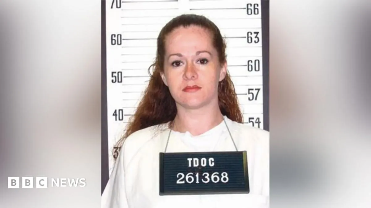 Christa Pike stands in front of a height measurement sign wearing a prison identification placard